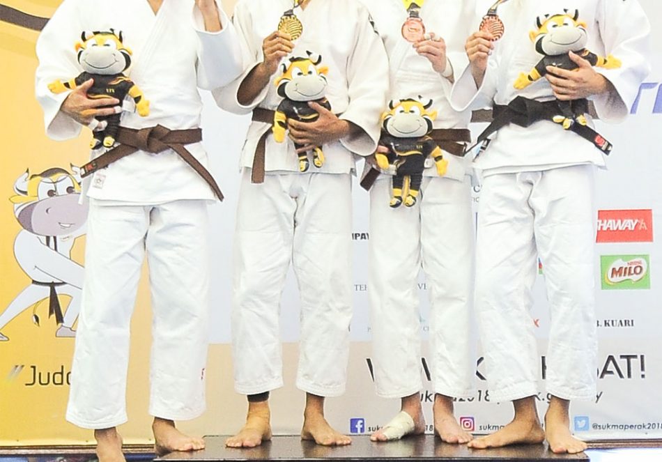 Muhammad Izham bin Harun(dua dari kiri) menyumbang pingat emas kepada kontijen Terengganu Hanelang setelah berentap dalam kategori lelaki bawah 60kg menewaskan judoka Negeri Sembilan; Toh Wei Sheng(kiri) di hari pertama kejohanan judo Sukan Malaysia(SUKMA) Perak 2018 yang telah berlansung di Dewan SMJK Krian, Kerian. Kredit Foto - Sekretariat SUKMA Perak 2018